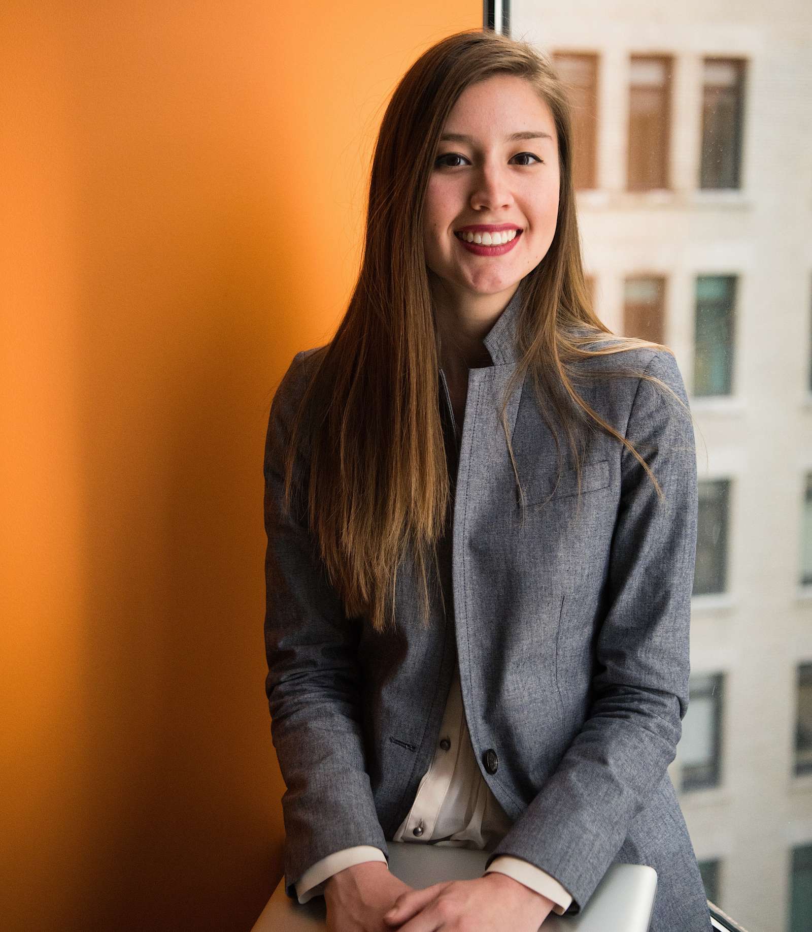 Dame im grauen Blazer vor orangefarbener Wand